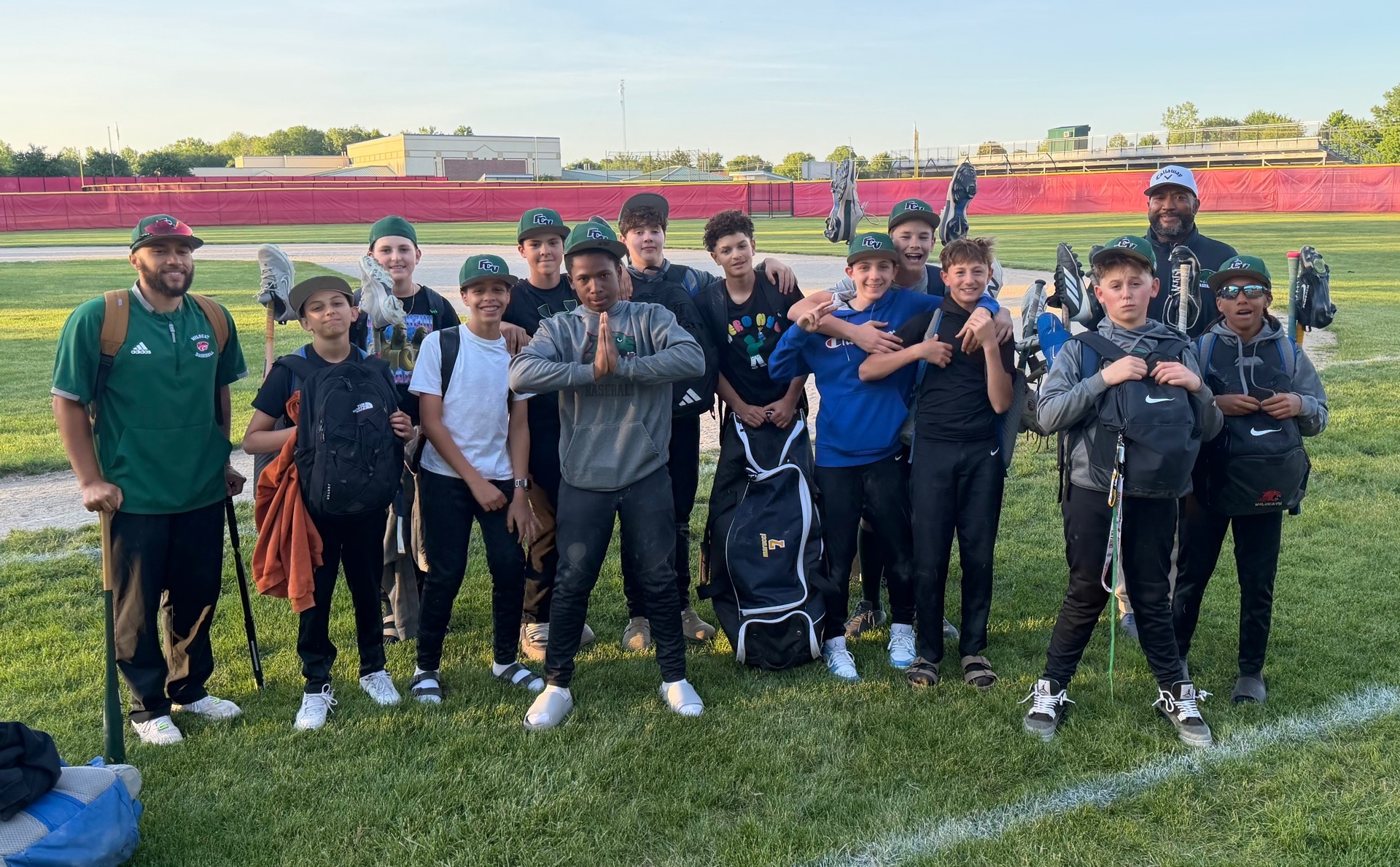 A group with baseball equipment poses beside an athletic field.