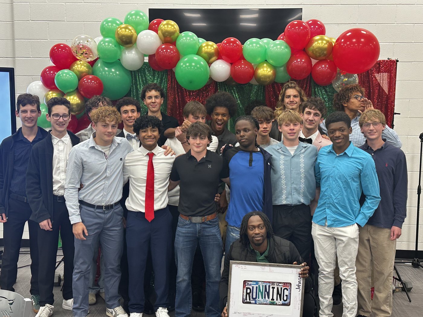 A group poses beneath colorful balloons, with a framed running-themed display.