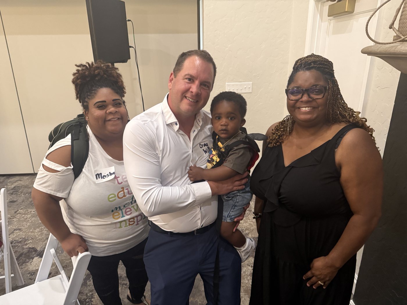 Three adults pose together indoors, with one holding a young child.