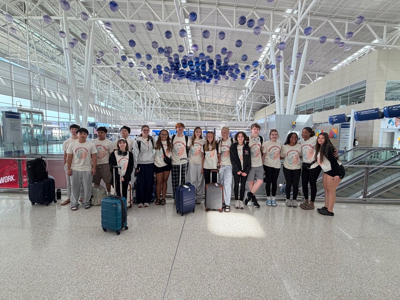 A group in matching shirts poses with luggage inside an airport terminal.